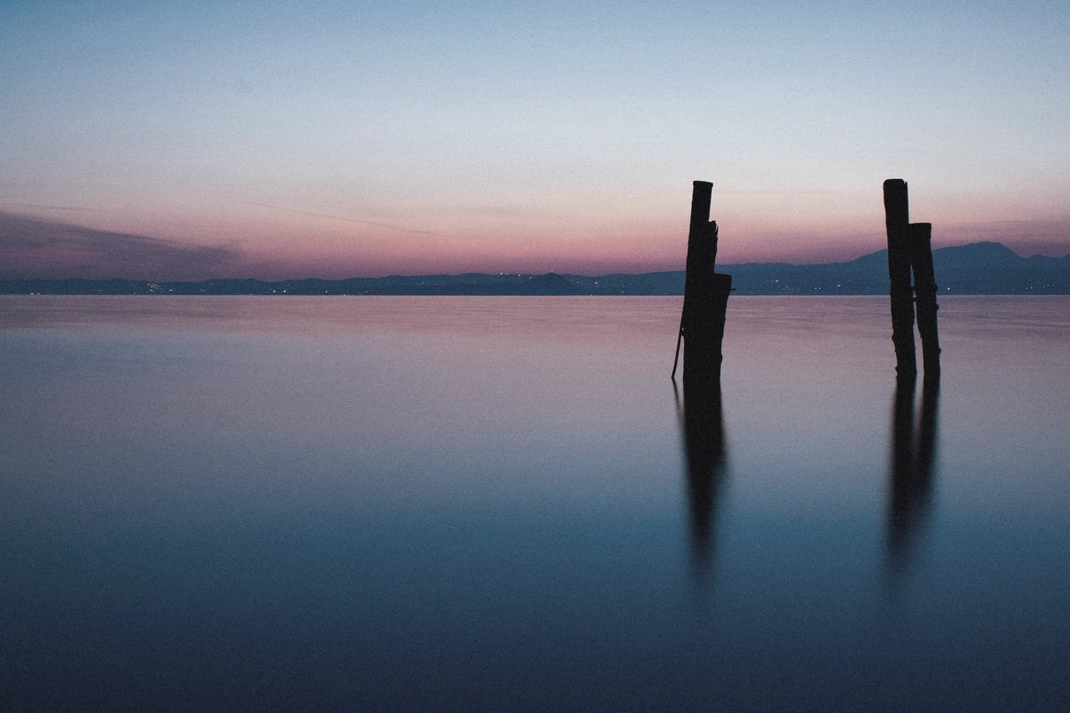 Old pier posts standing in a still lake at dusk, the sky fading from pink to blue.