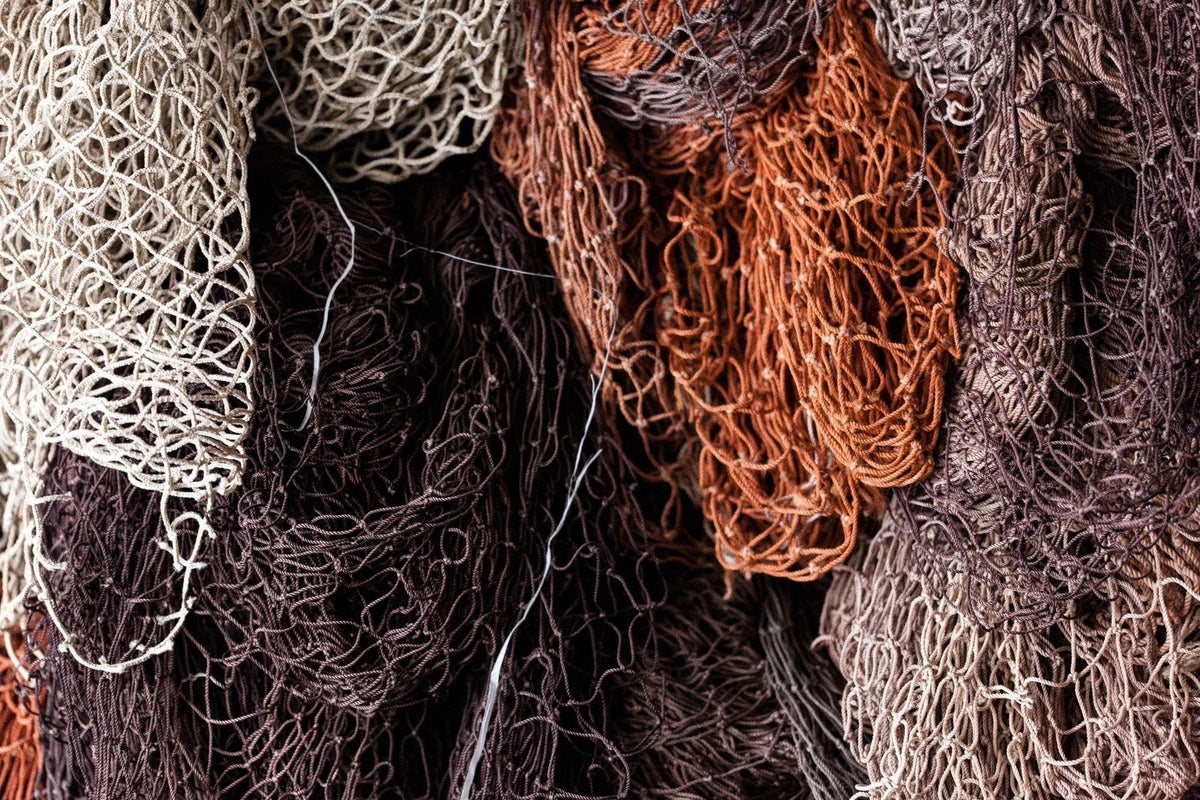 Recovered fishing nets in white, rust and brown, piled for regeneration.