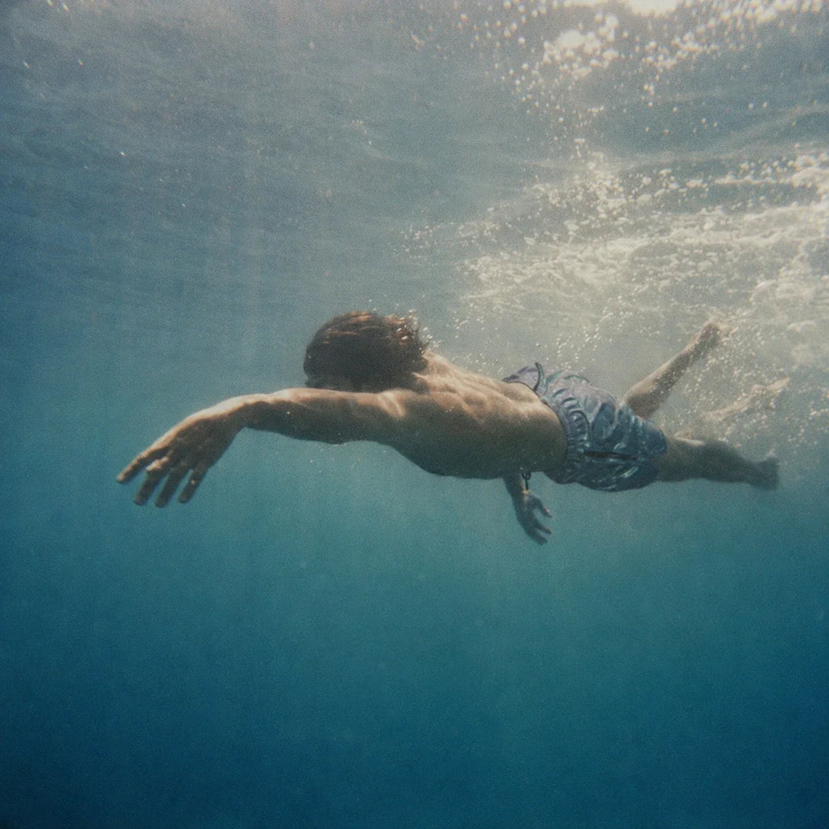A swimmer gliding underwater in green-blue open water.