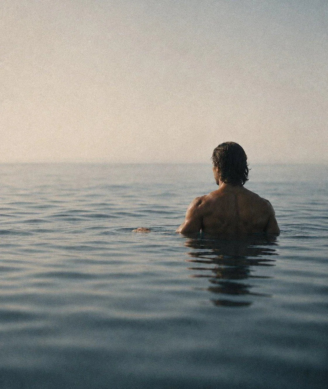 A swimmer standing chest-deep in calm open water, looking out before the first stroke.