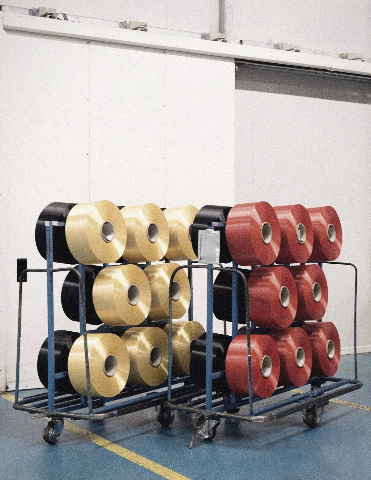 Spools of yellow, red and black yarn stacked on trolleys on a mill floor.