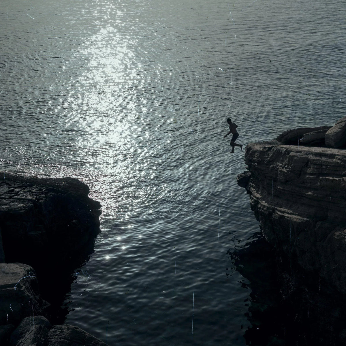A swimmer jumping from dark rocks into sunlit water.